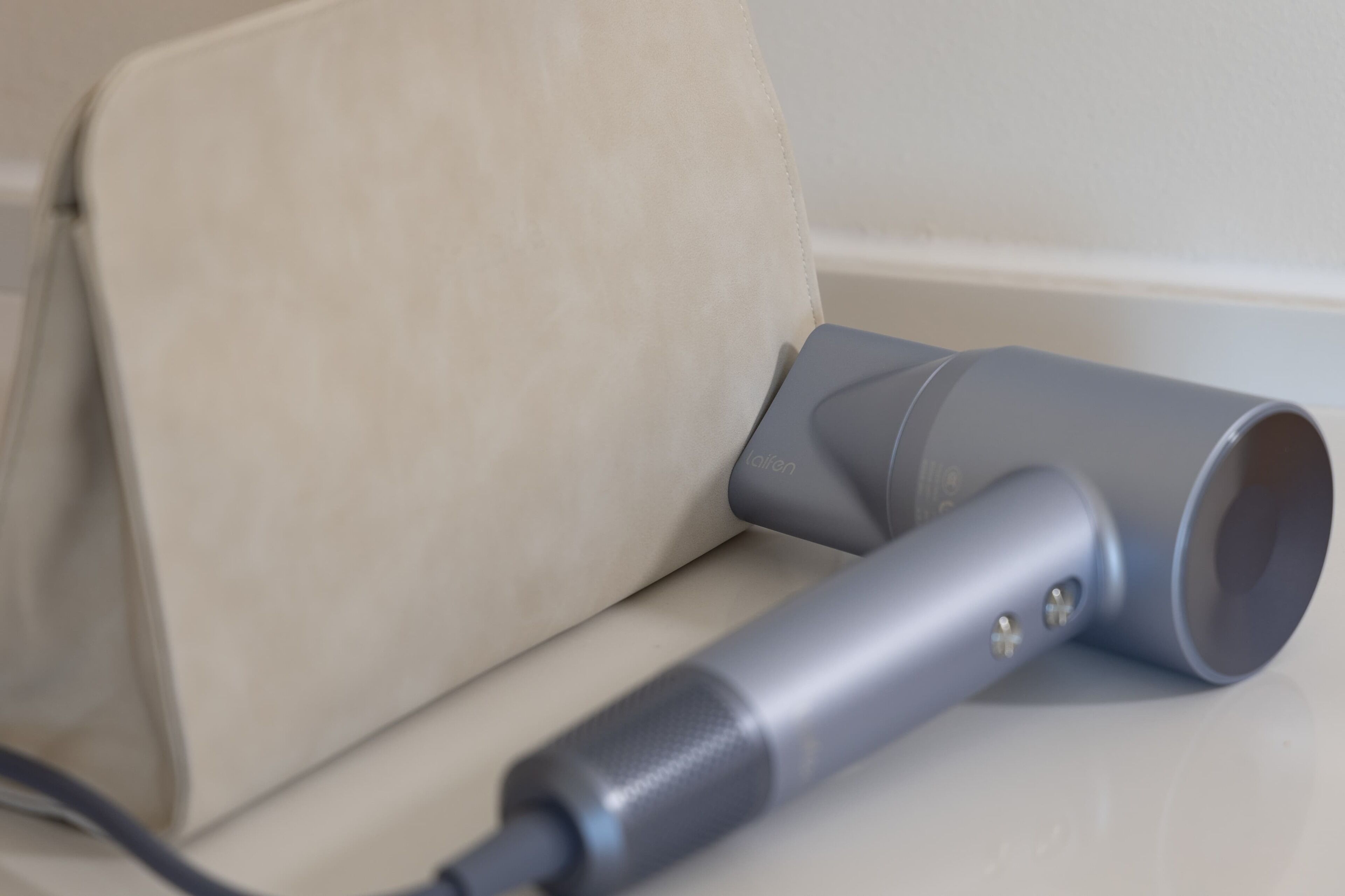 A grey portable speaker with a cable, placed on a beige surface.