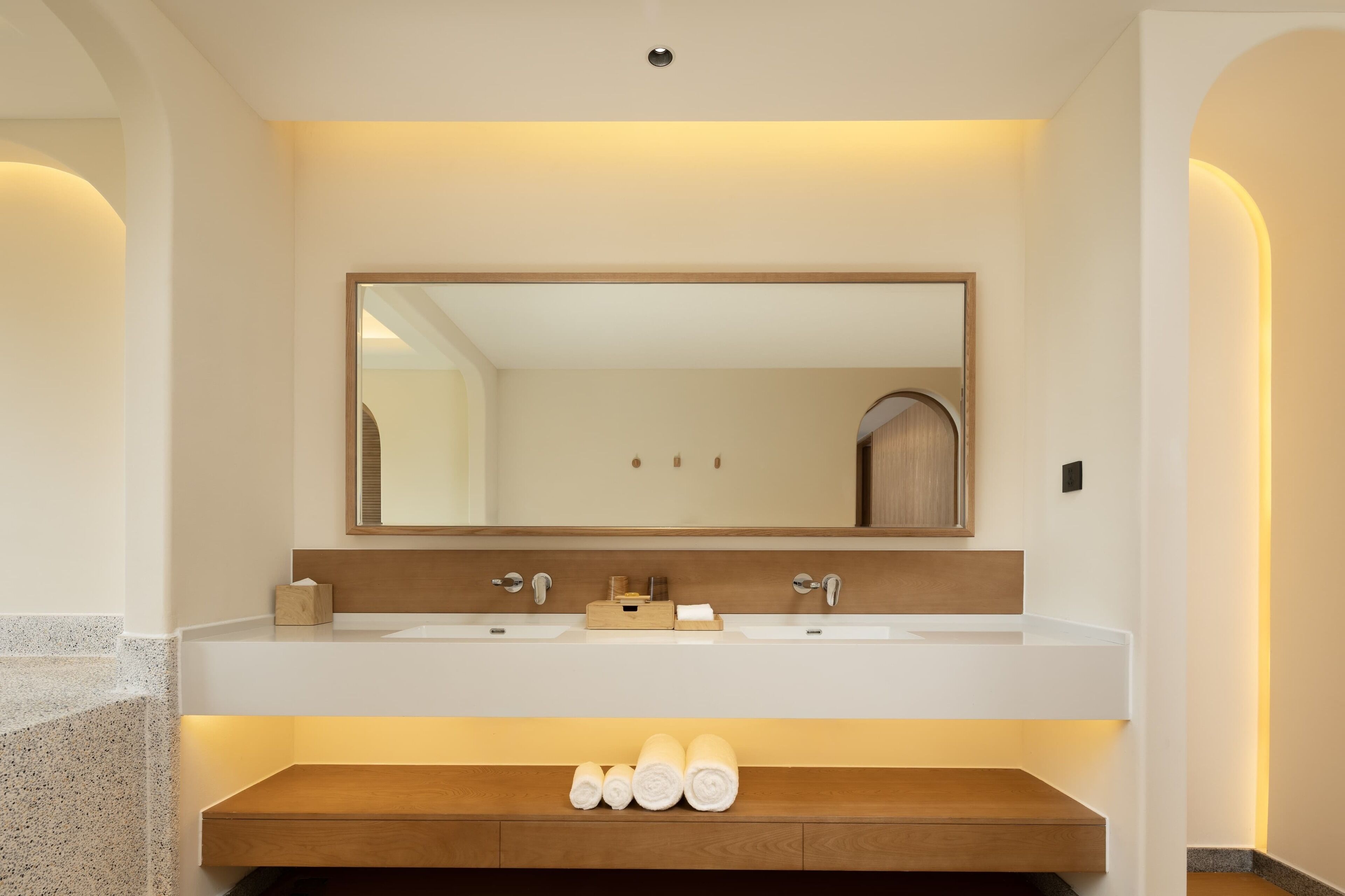 A modern bathroom with a large mirror, two sinks, and a wooden vanity with towels.
