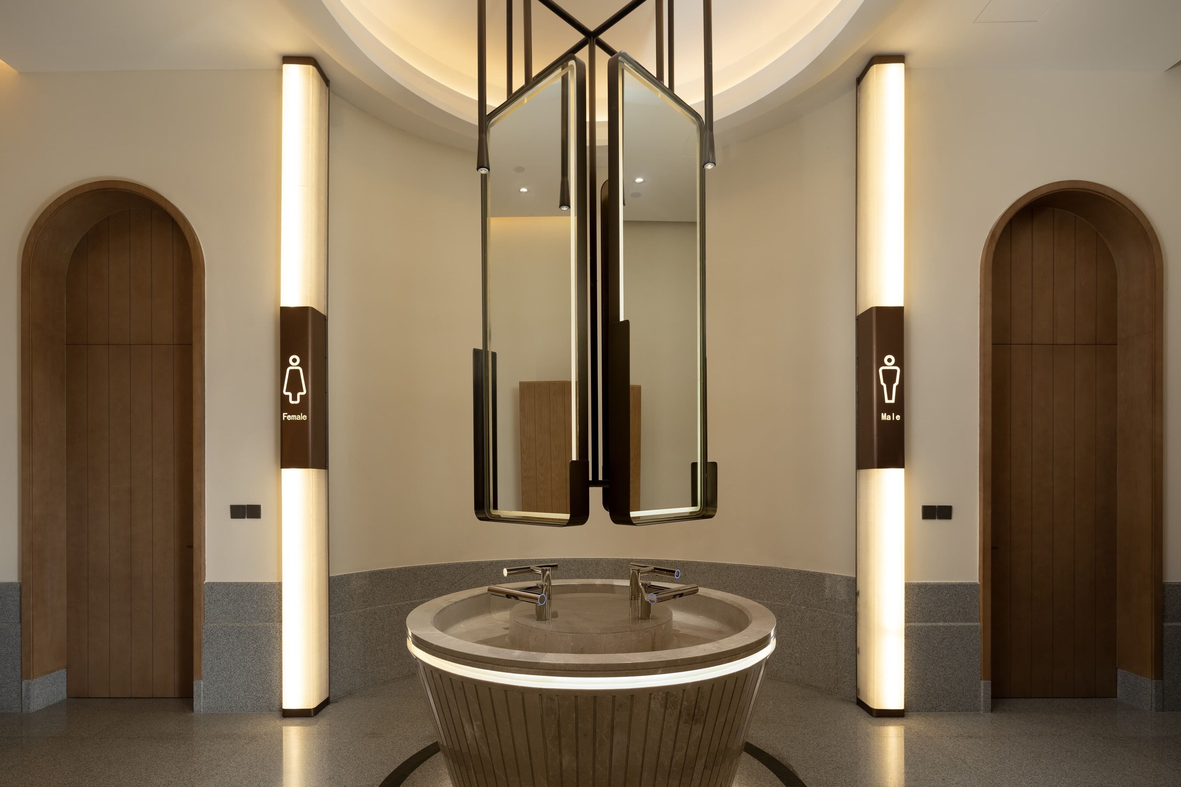 A modern bathroom with a central sink, two mirrors, and gender-specific signs above the mirrors.
