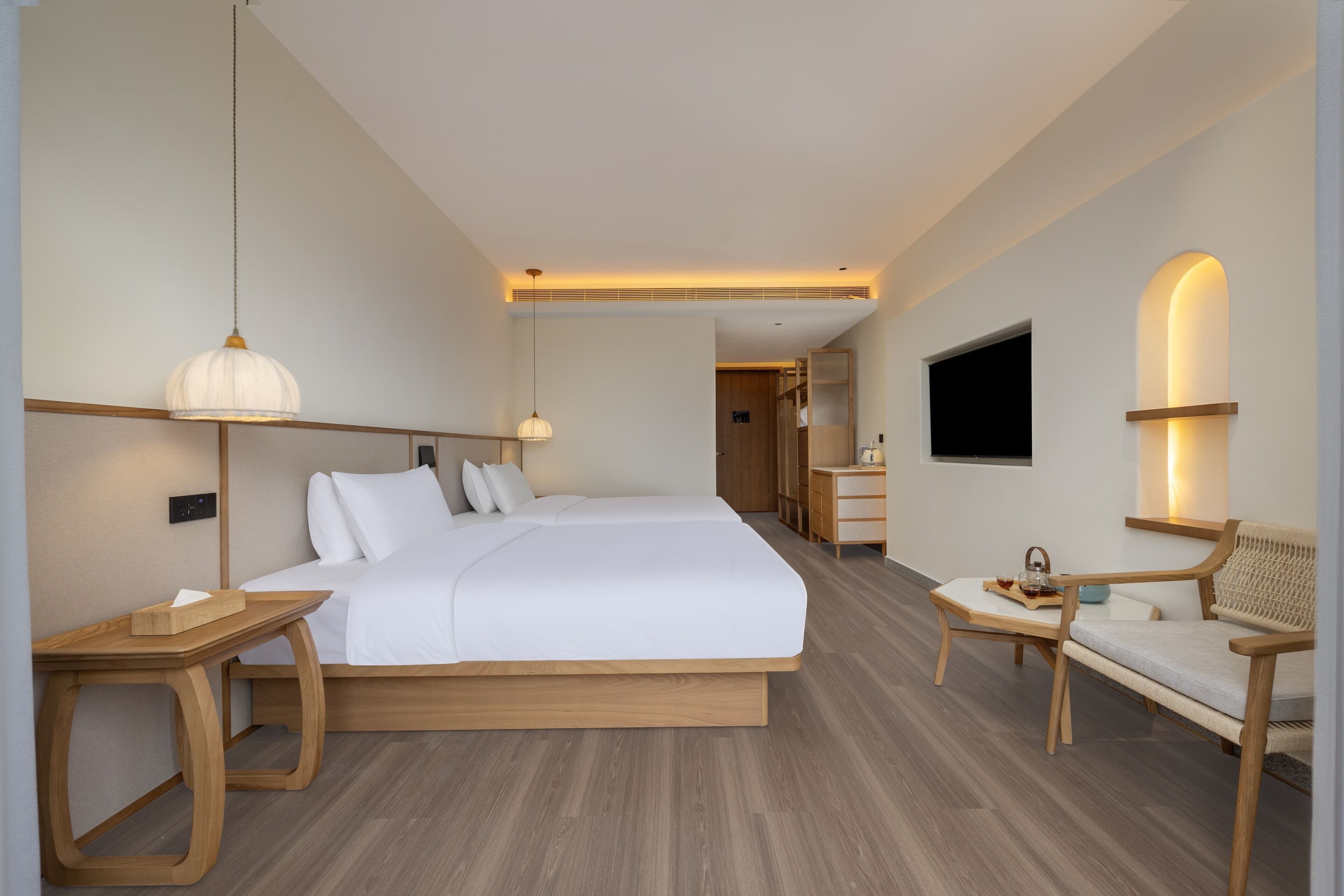 Une chambre d’hôtel moderne dotée d’un grand lit, de tables de chevet, d’un coin salon avec une chaise et une table, d’un téléviseur fixé au mur et d’un plancher en bois.