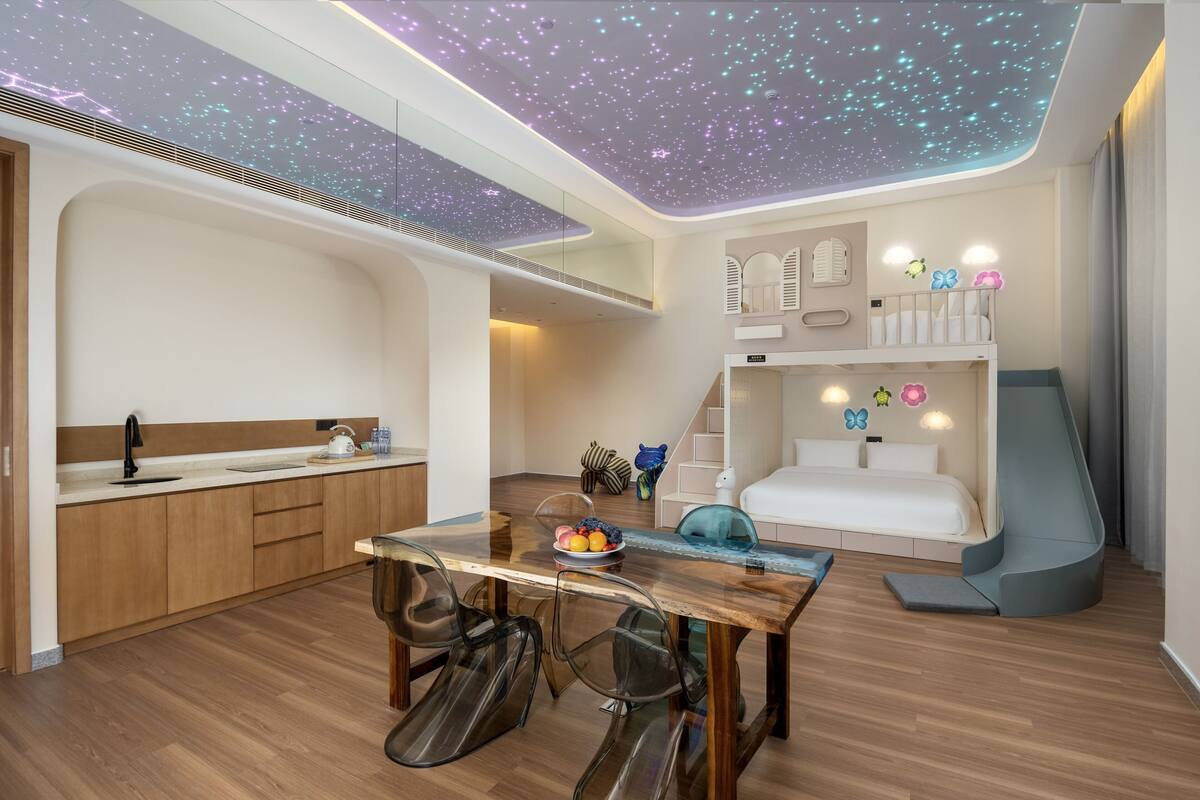 A modern room with a starry ceiling, a wooden dining table, a kitchen area, and a cozy sleeping area with a slide.