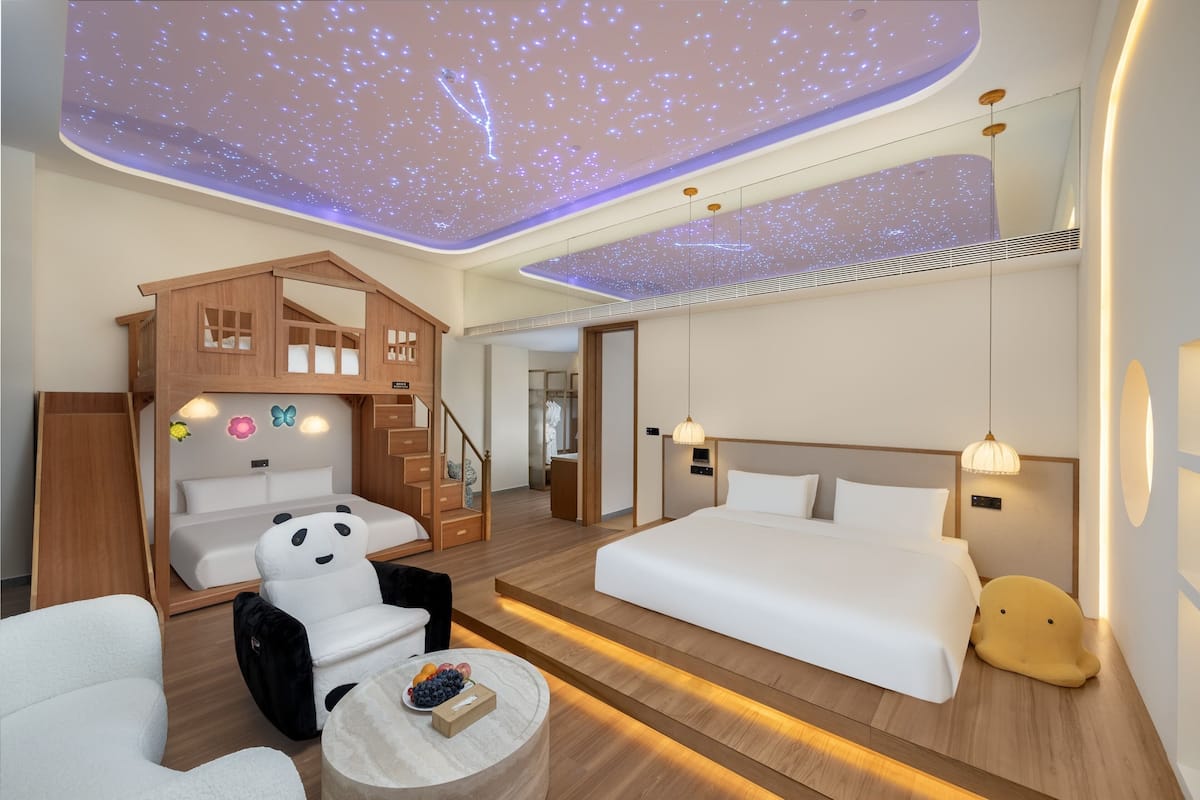 A modern hotel room with a starry ceiling, a cozy playhouse, a large bed, and a comfortable seating area.