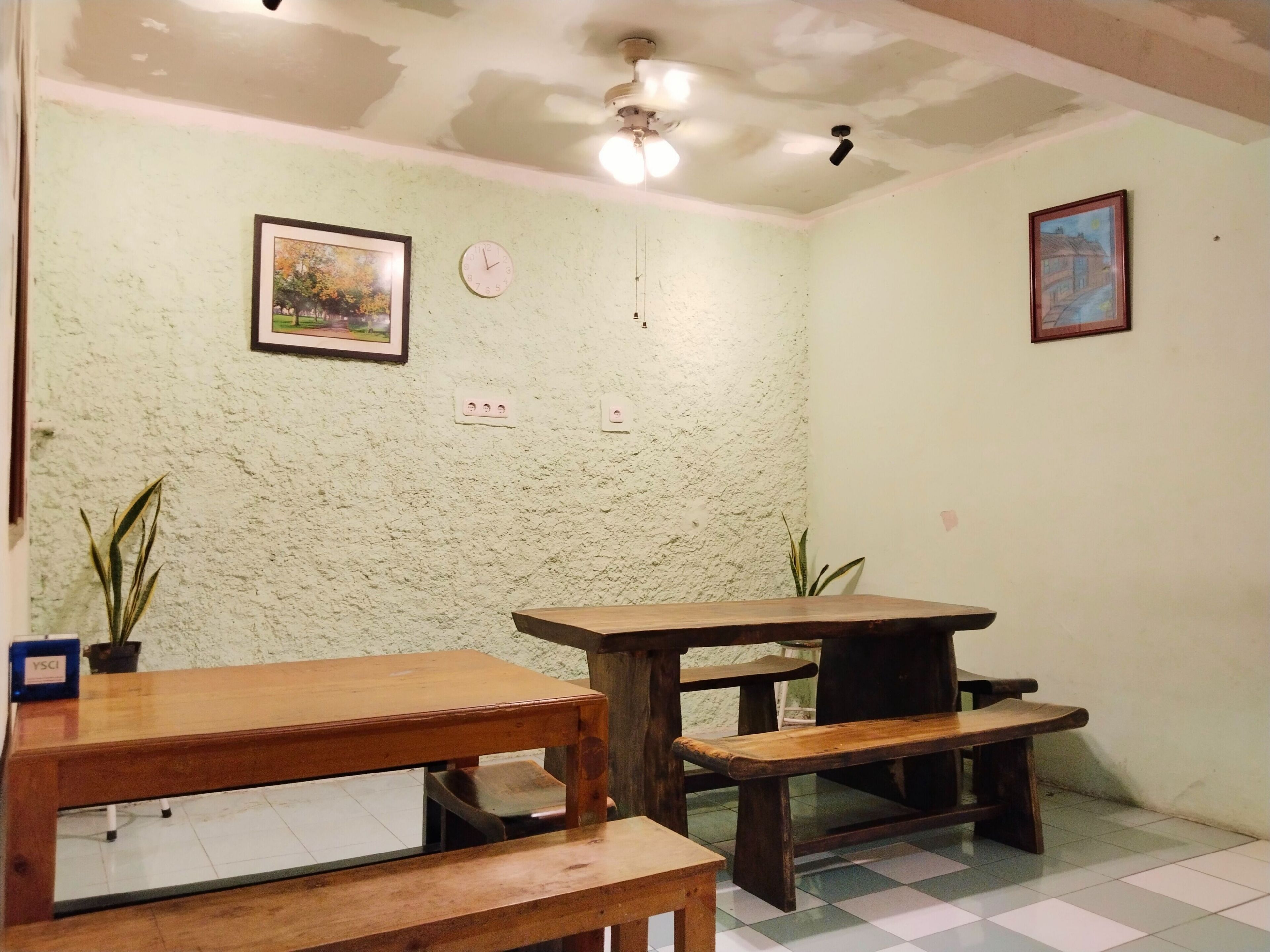 A room with a green textured wall, a ceiling fan, two wooden tables, and two benches.