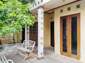 A courtyard with a white metal bench, a tree, and a building entrance with a glass door. - Homestay Famili Taqwa (Jakarta)