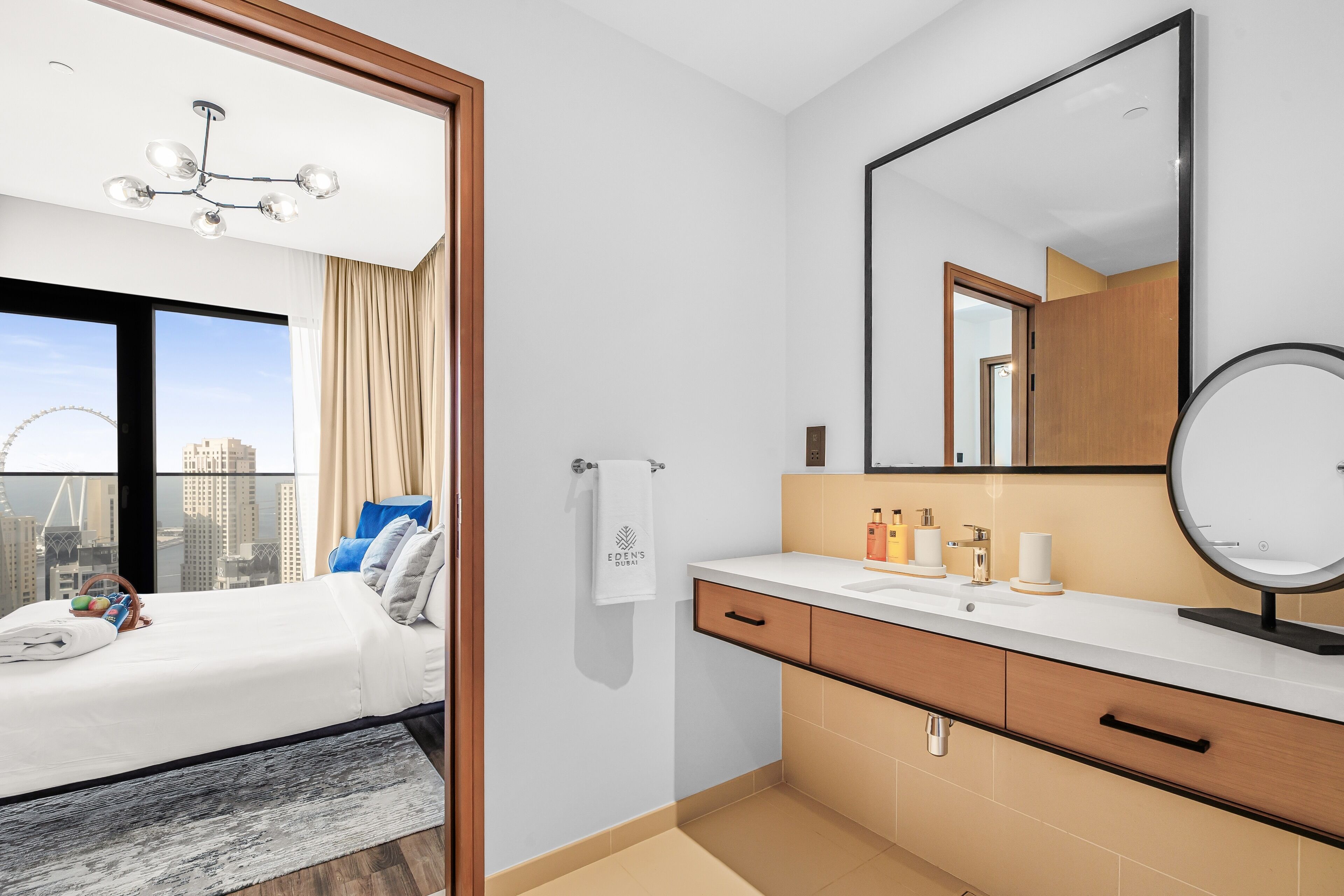 Una habitación de hotel moderna con una cama grande, un baño con tocador y espejo, y vistas a la ciudad.
