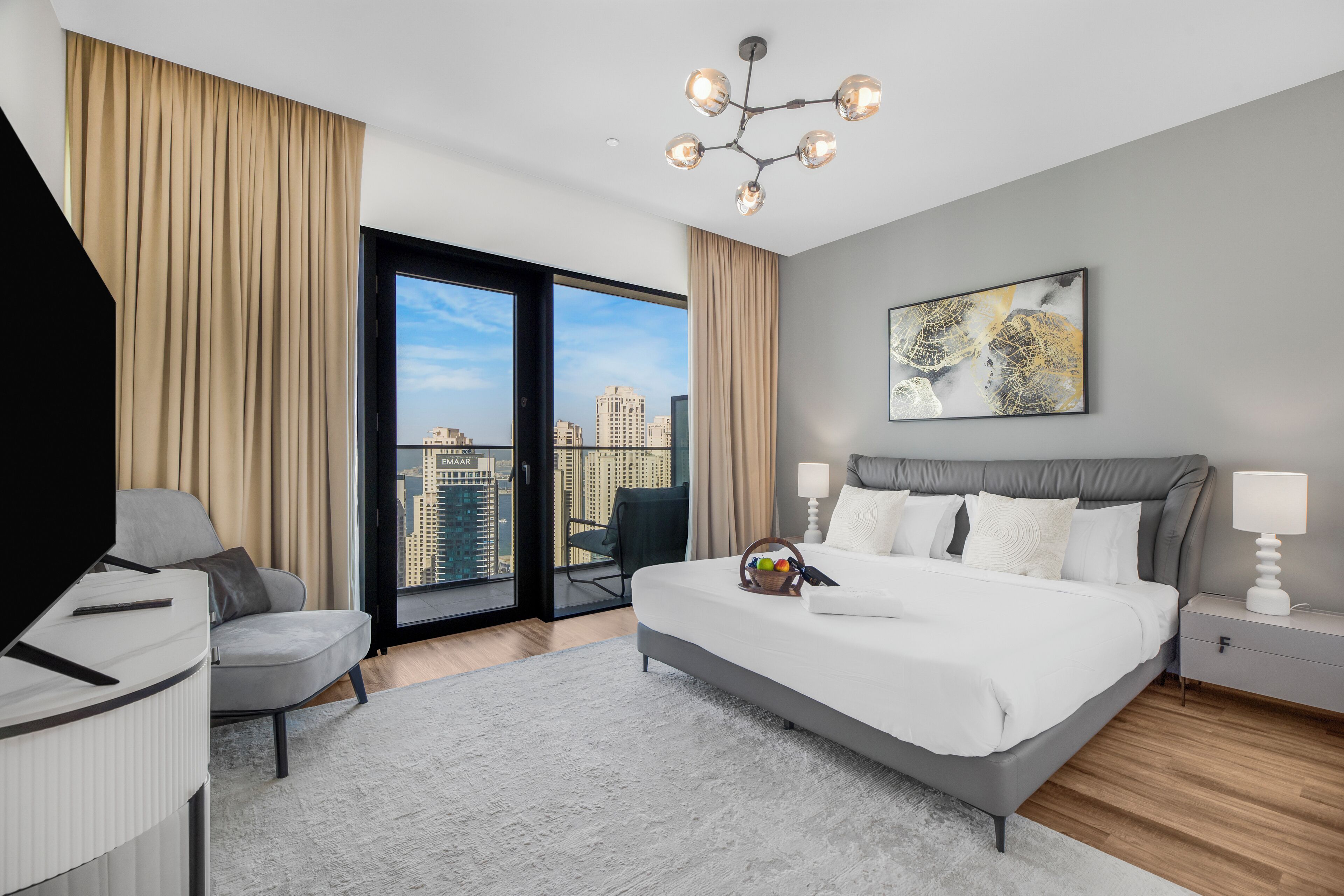 Ein modernes Hotelzimmer mit einem großen Bett, einem Schreibtisch, einem Sessel und Blick auf die Stadt durch eine Glastür.