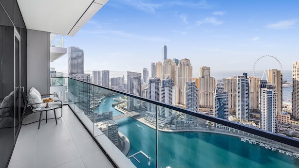 A balcony with a glass railing overlooking a cityscape with high-rise buildings and a body of water. - EDEN’S Homes & Villas - VIDA Dubai Marina Residences (Dubai)
