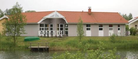 A two-story building with a red-tiled roof, a covered porch, and a dock extending into a body of water.