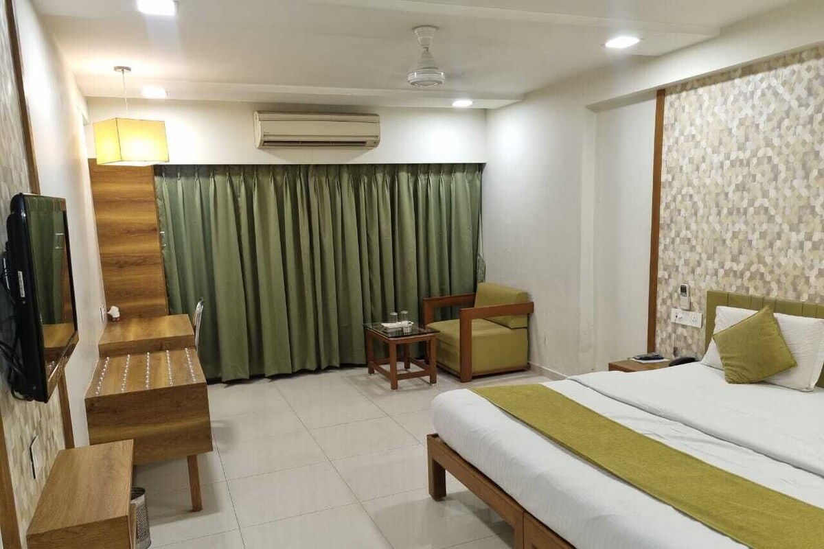 A hotel room with a bed, a desk, a chair, a small table, and a television.