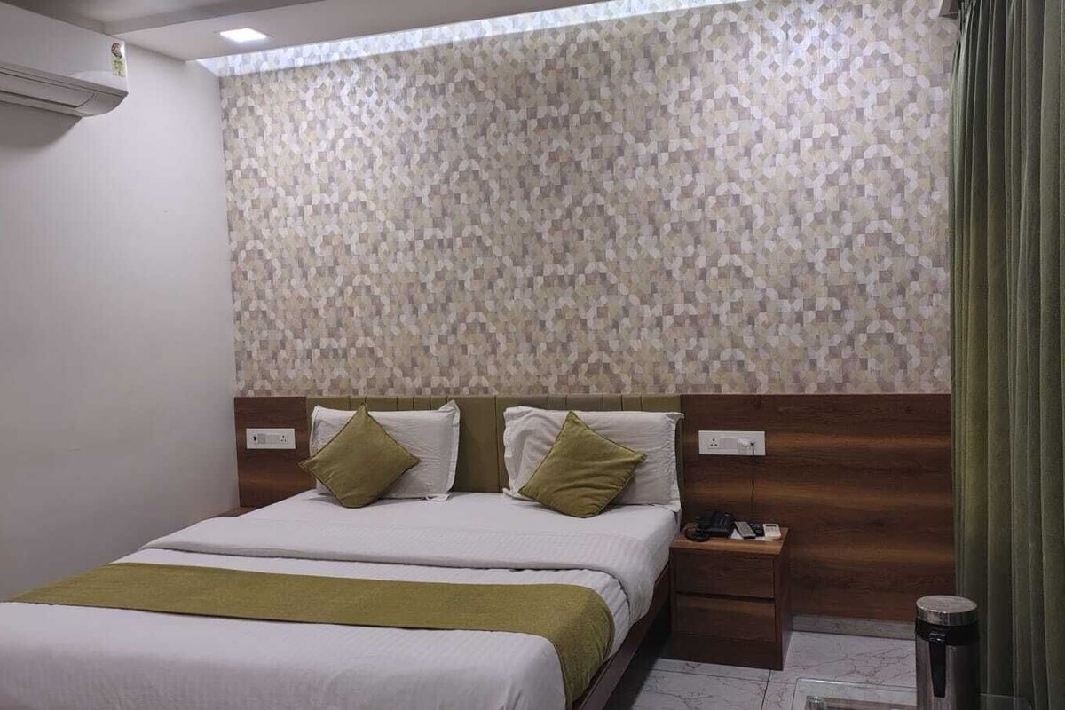 A hotel room with a bed, a nightstand, a wall-mounted air conditioner, and a curtain.