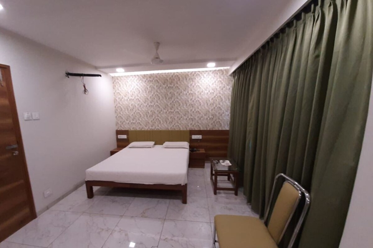 A bedroom with a bed, a nightstand, a chair, a wooden wardrobe, and a curtain.