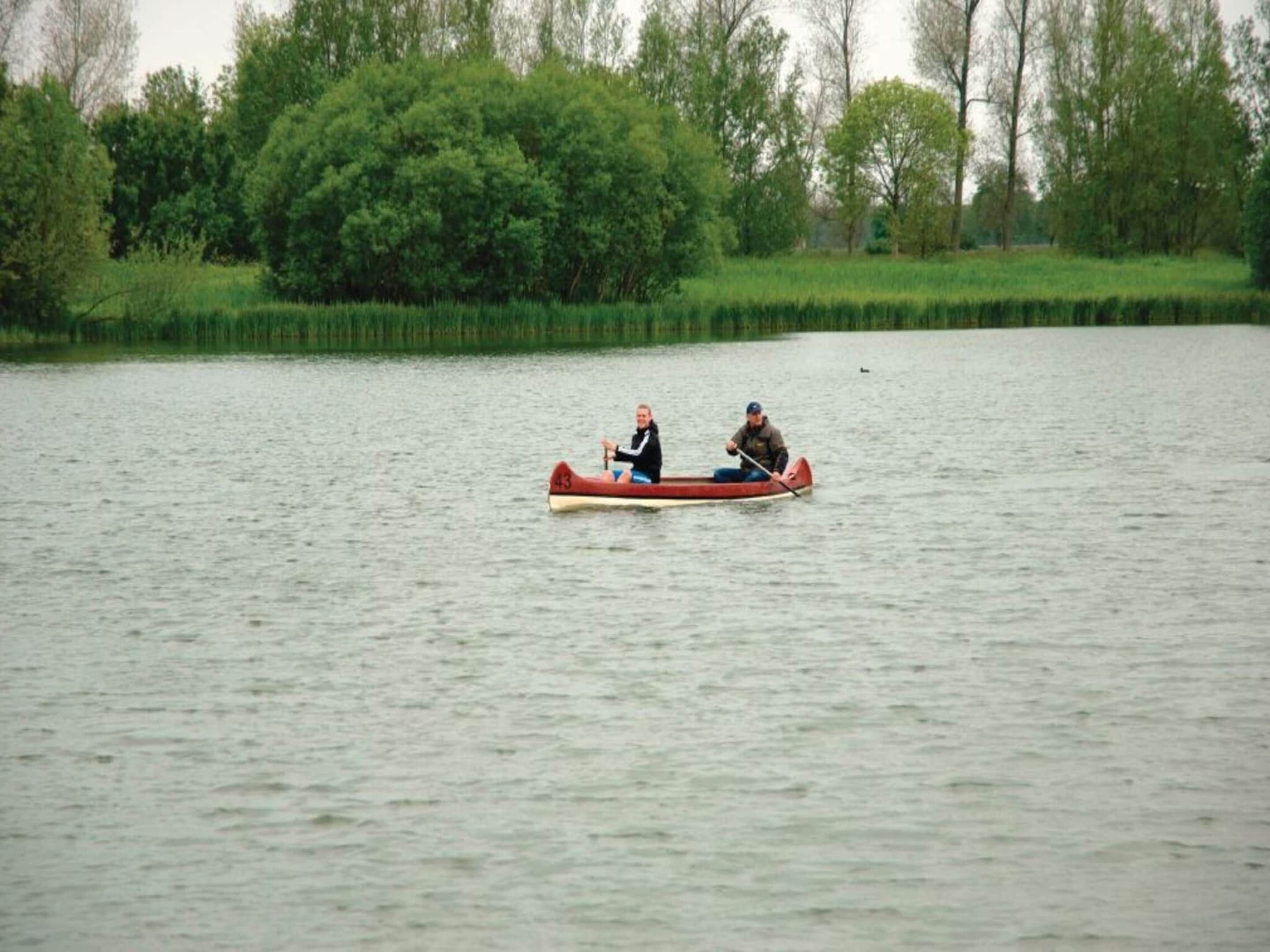 Two people in a red canoe on a calm lake with trees in the background.