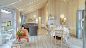 A spacious living area with a high ceiling, wooden walls, a dining table set for six, and a comfortable seating area with a sofa and chairs. - 4 Star Holiday Home in Ottendorf (Otterndorf)