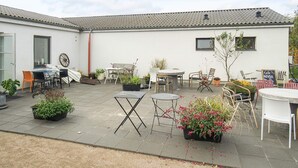 A courtyard with outdoor seating, potted plants, and a building with a tiled roof. - Holiday Home in Nature (Gørlev)