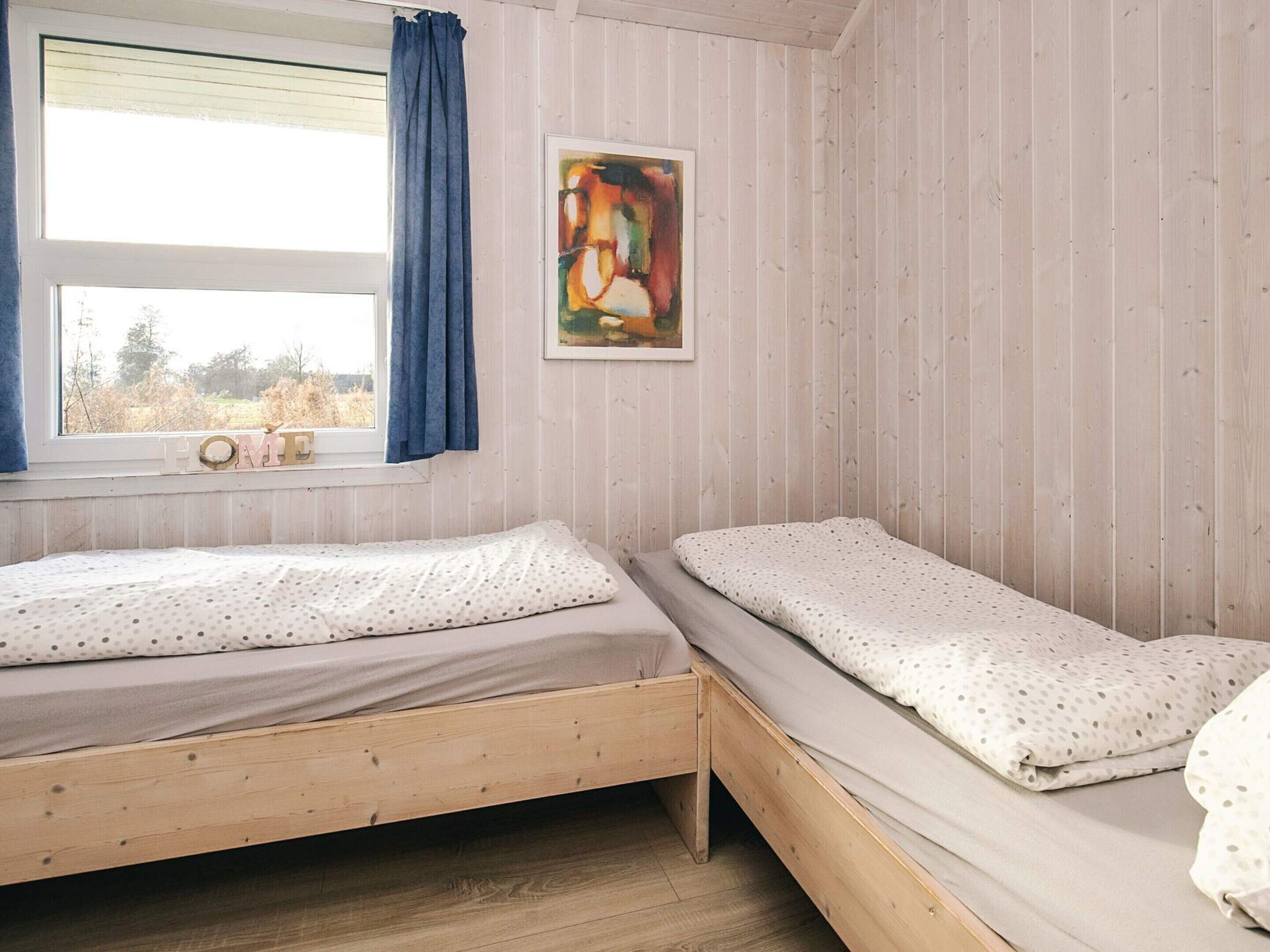 A bedroom with two wooden beds, a window with blue curtains, and a framed abstract painting on the wall.