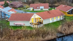 A lakeside property with multiple houses, including a prominent house with a large porch and a glassed-over section. - 4 Star Holiday Home in Ottendorf (Otterndorf)