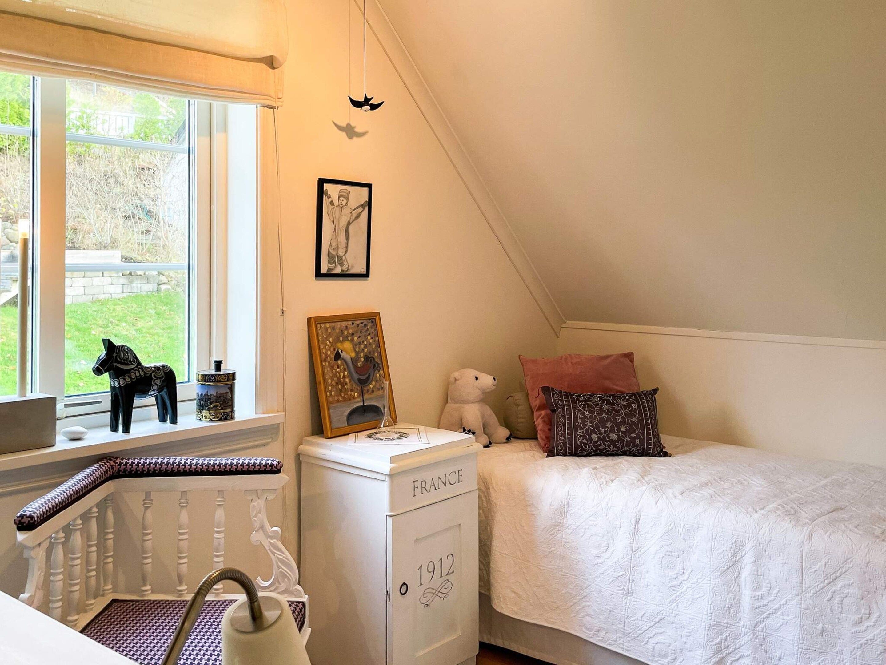 A bedroom with a window, a radiator, a chest of drawers, a bed, and a teddy bear.