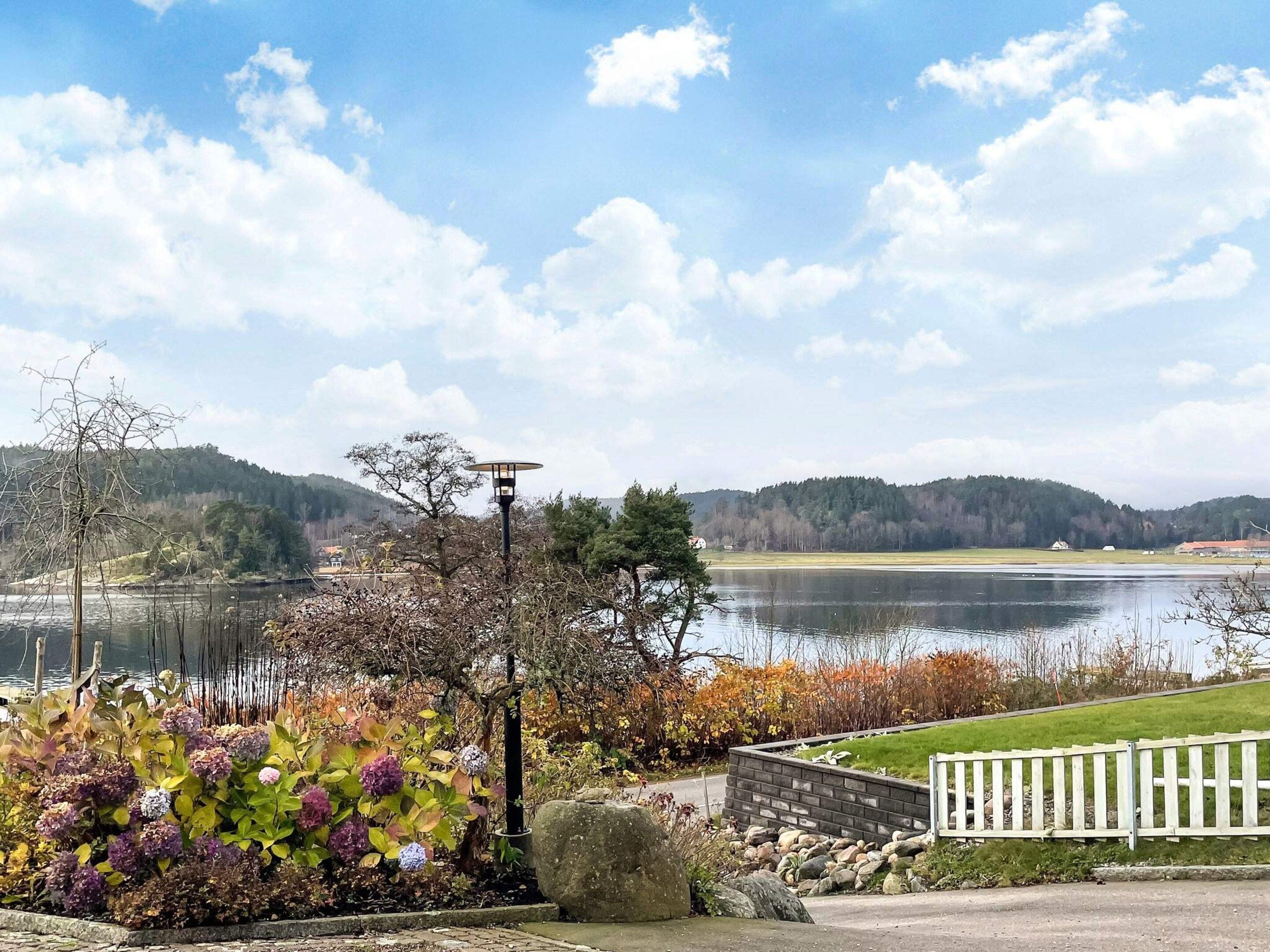 A lakeside view with a white fence, a lamp post, and a variety of shrubs.