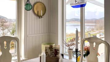 Quarto com mesa posta para refeições, vista para um lago e decoração náutica com um barco à vela suspenso.