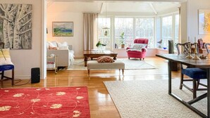 A spacious living room with a large window, a red floral rug, a pink armchair, and a dining area with a table and chairs. - 5 Star Holiday Home in Uddevalla (Uddevalla)