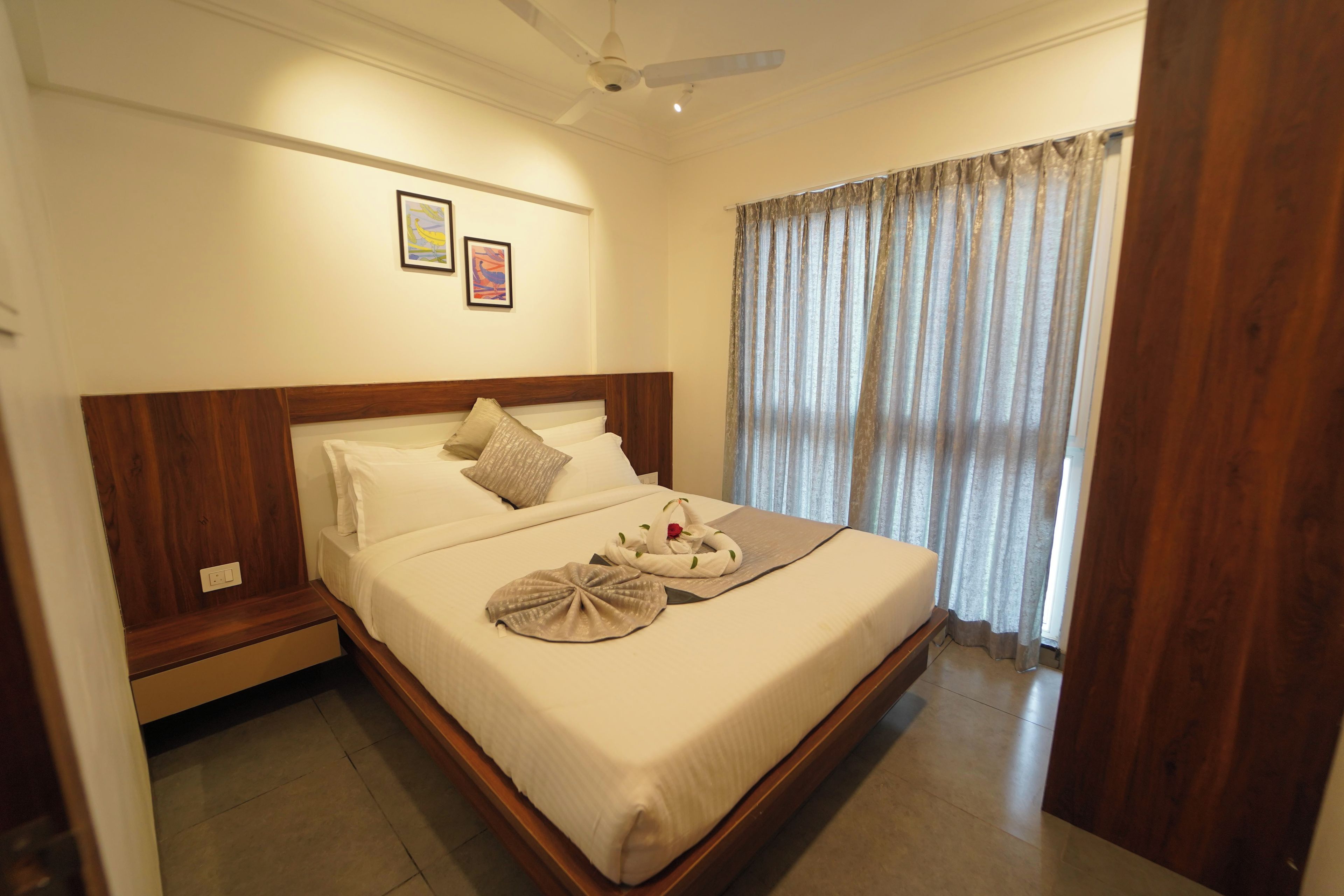 A hotel room with a large bed, a ceiling fan, and a window with curtains.