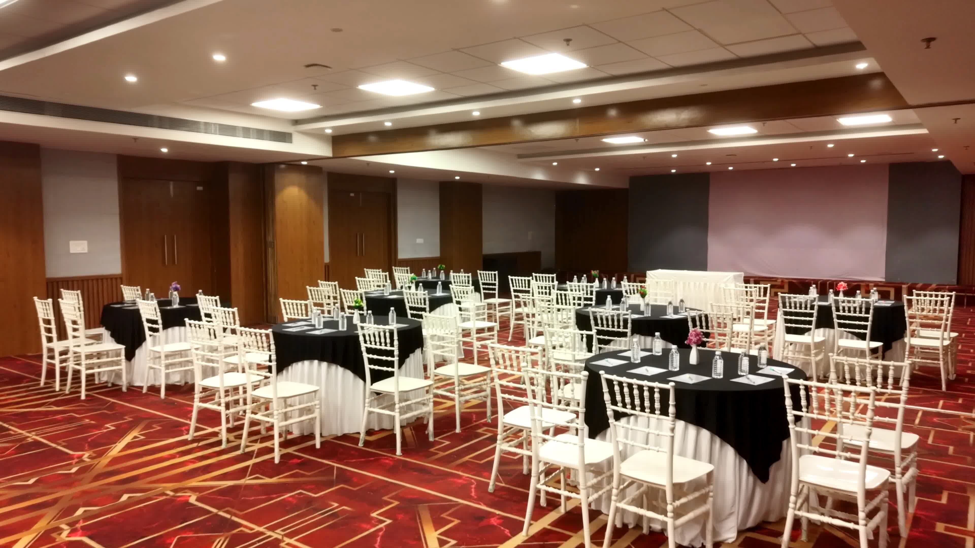 Un salón de conferencias con varias mesas redondas, sillas blancas y manteles negros.