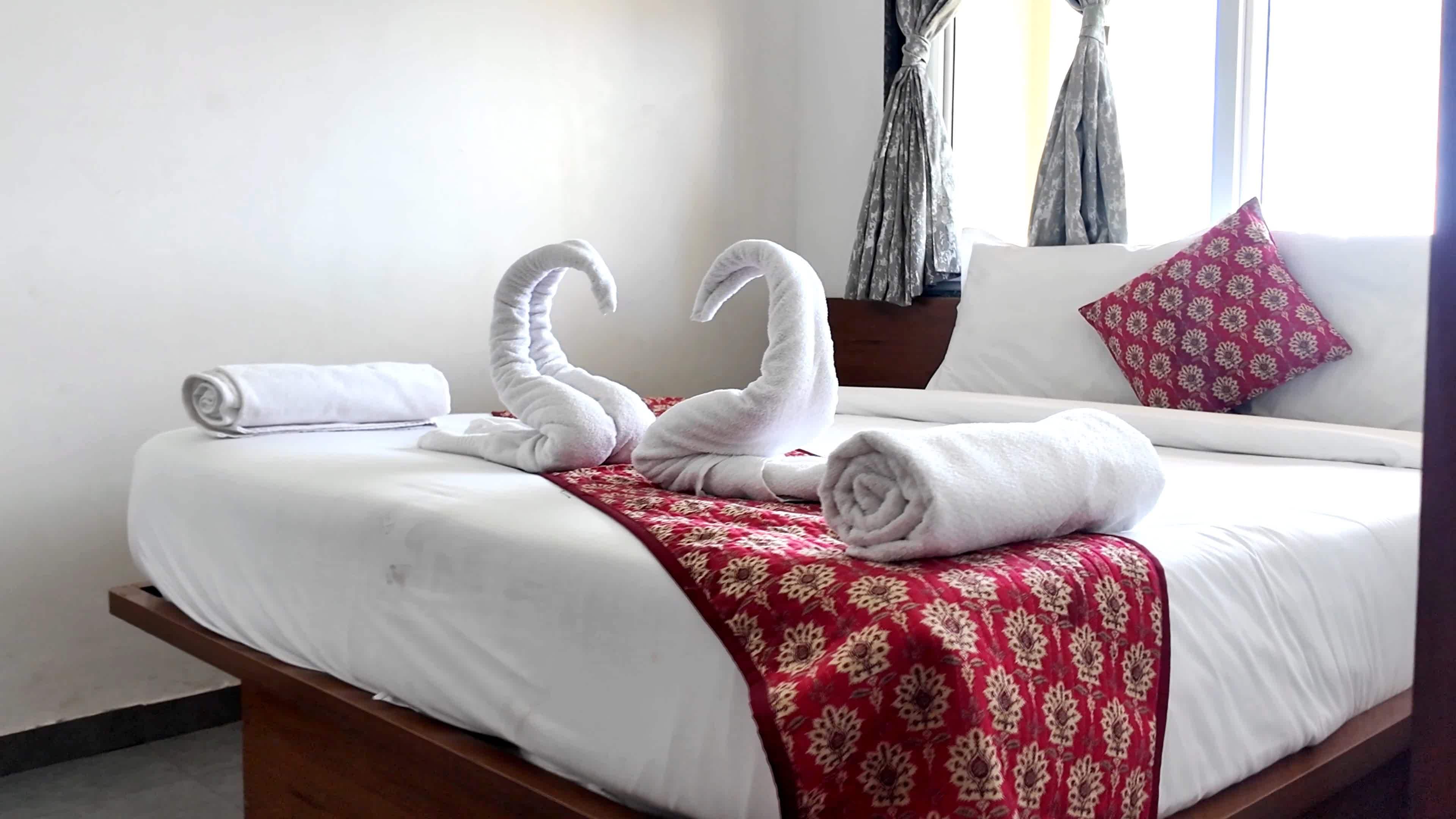 A hotel room with a bed, a red patterned throw, and a pillow with a floral design.