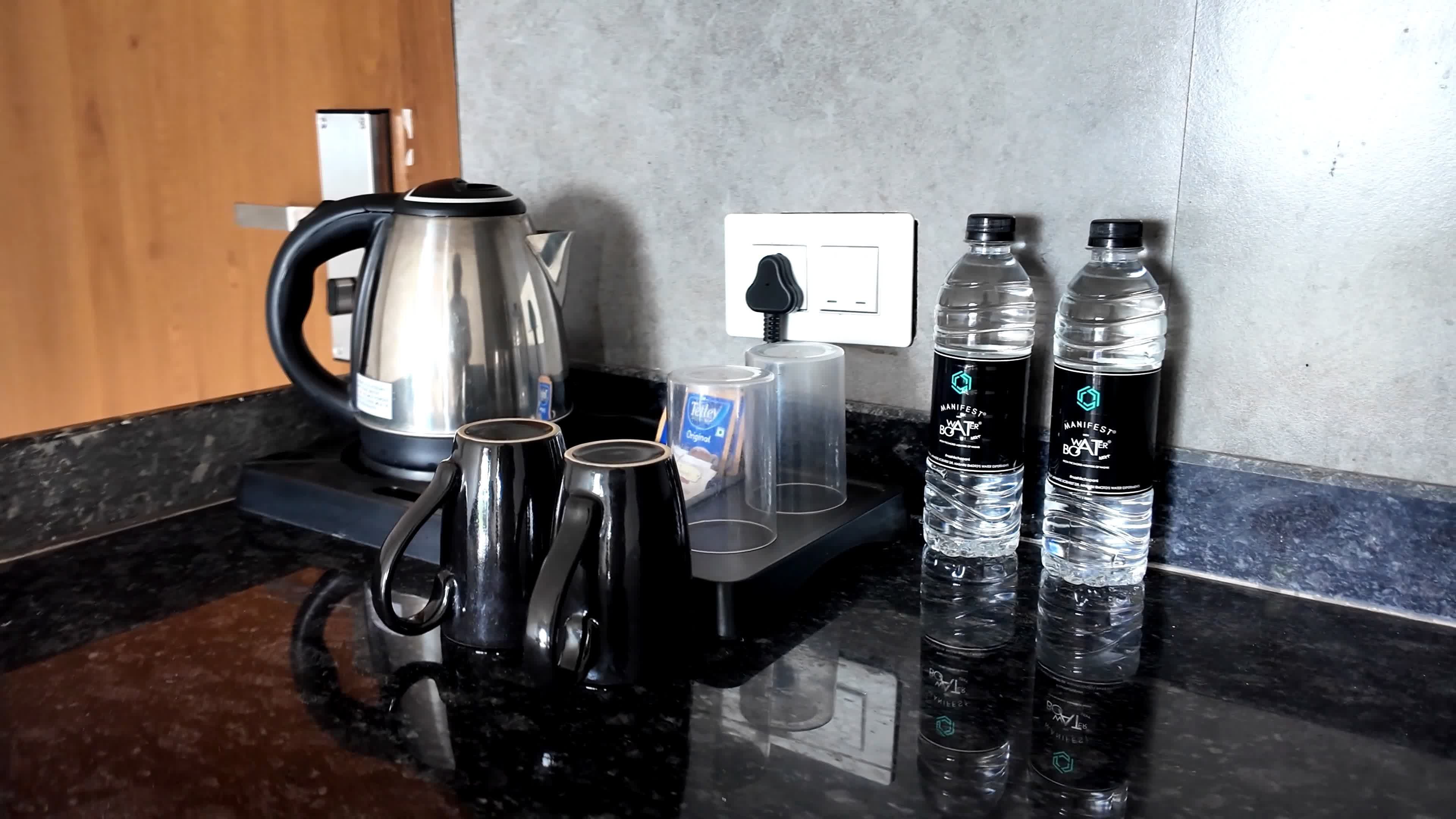 Eine Küchenarbeitsplatte mit einem Wasserkocher, zwei Tassen, einer Kaffeekapsel und zwei Wasserflaschen.