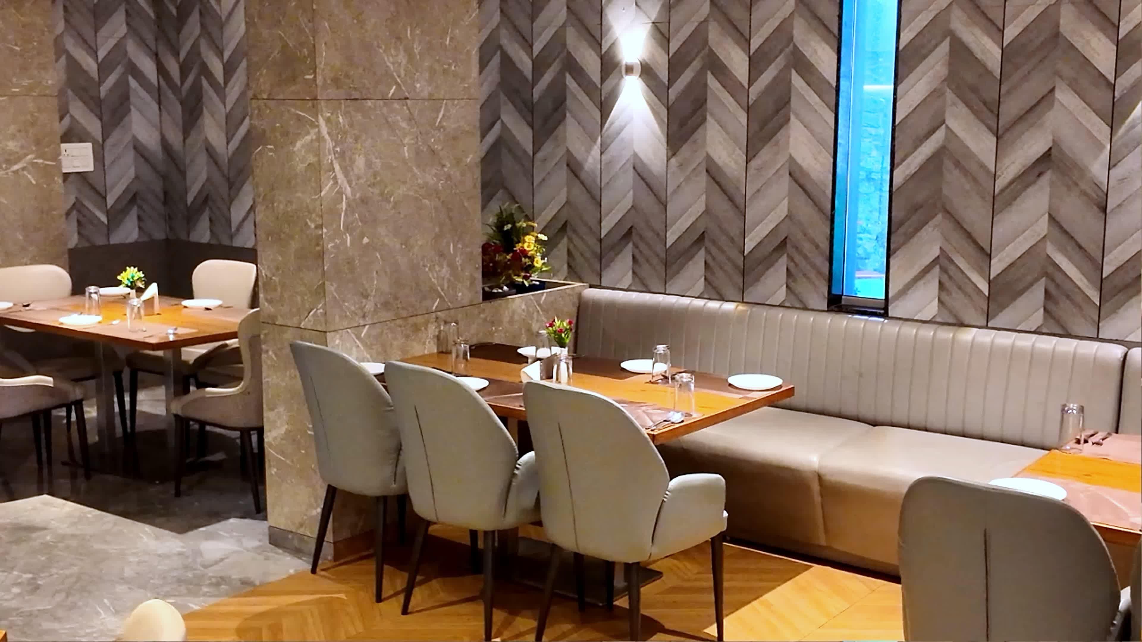 A modern dining area with a herringbone-patterned wall, a wooden floor, and a seating arrangement that includes a long table and a cushioned bench.