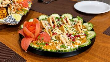 A round black plate with a salad, grilled chicken, and vegetables on a wooden table.