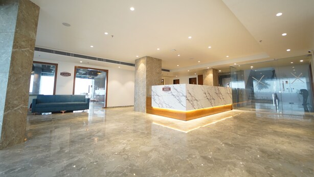 Een moderne lobby met een marmeren receptiebalie, een blauwe bank en een glazen scheidingswand.