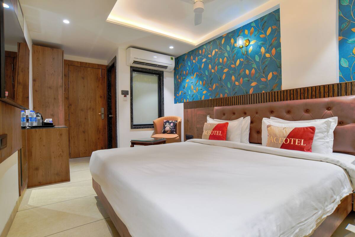 A hotel room with a large bed, a wooden wardrobe, a seating area with a chair, and a wall with a leaf pattern.