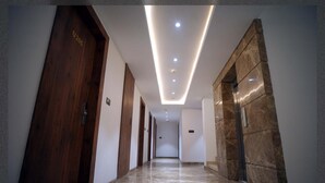 A modern hotel corridor with wooden doors, marble flooring, and recessed lighting. - Hotel Guru Kripa, Bhopal (Bhopal)