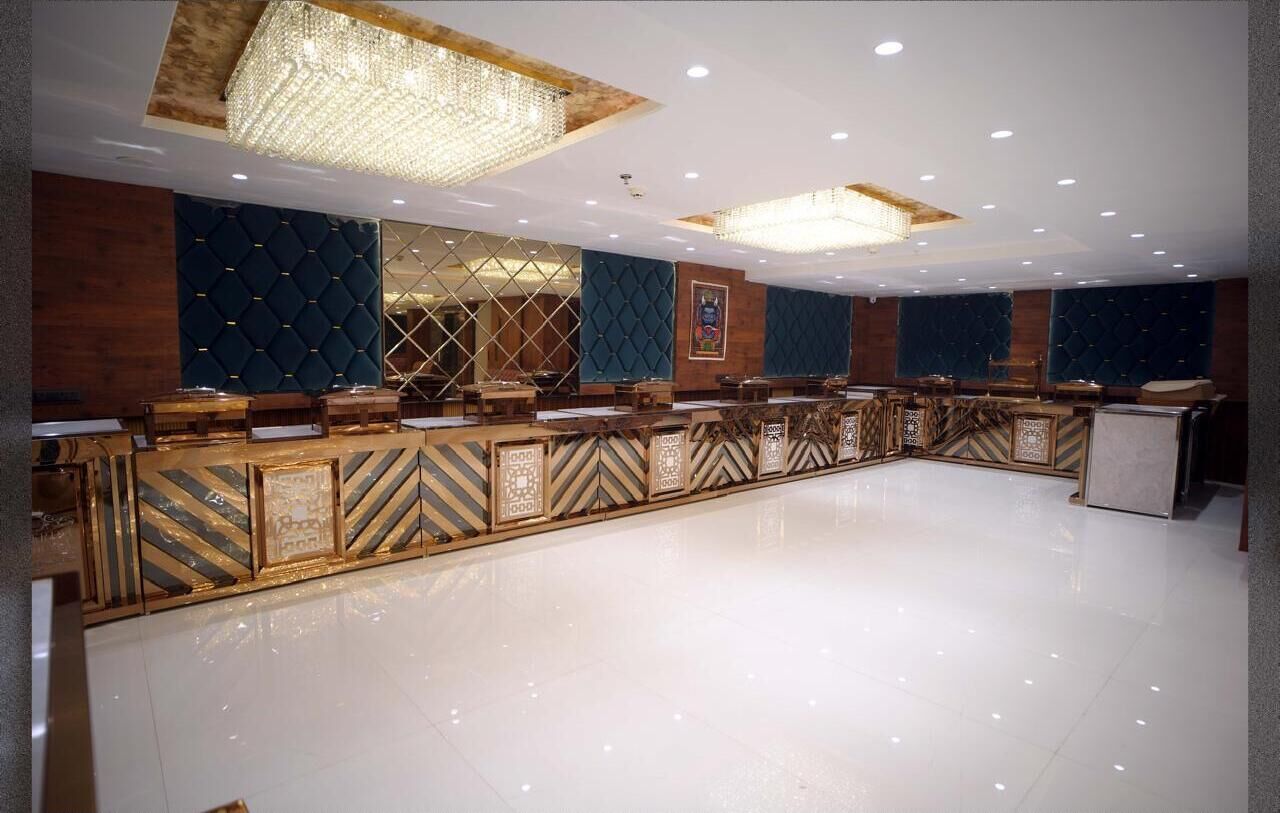 A spacious hotel lobby with a long reception desk, modern chandeliers, and a polished floor.