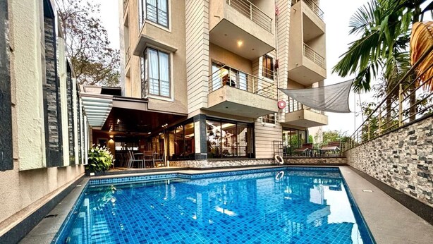 A swimming pool with a tiled deck, surrounded by a building with balconies and a restaurant area.