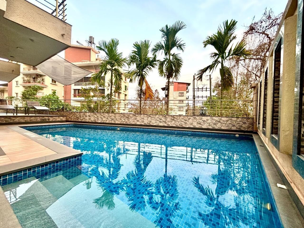 A swimming pool with clear blue water, surrounded by a stone wall and palm trees.