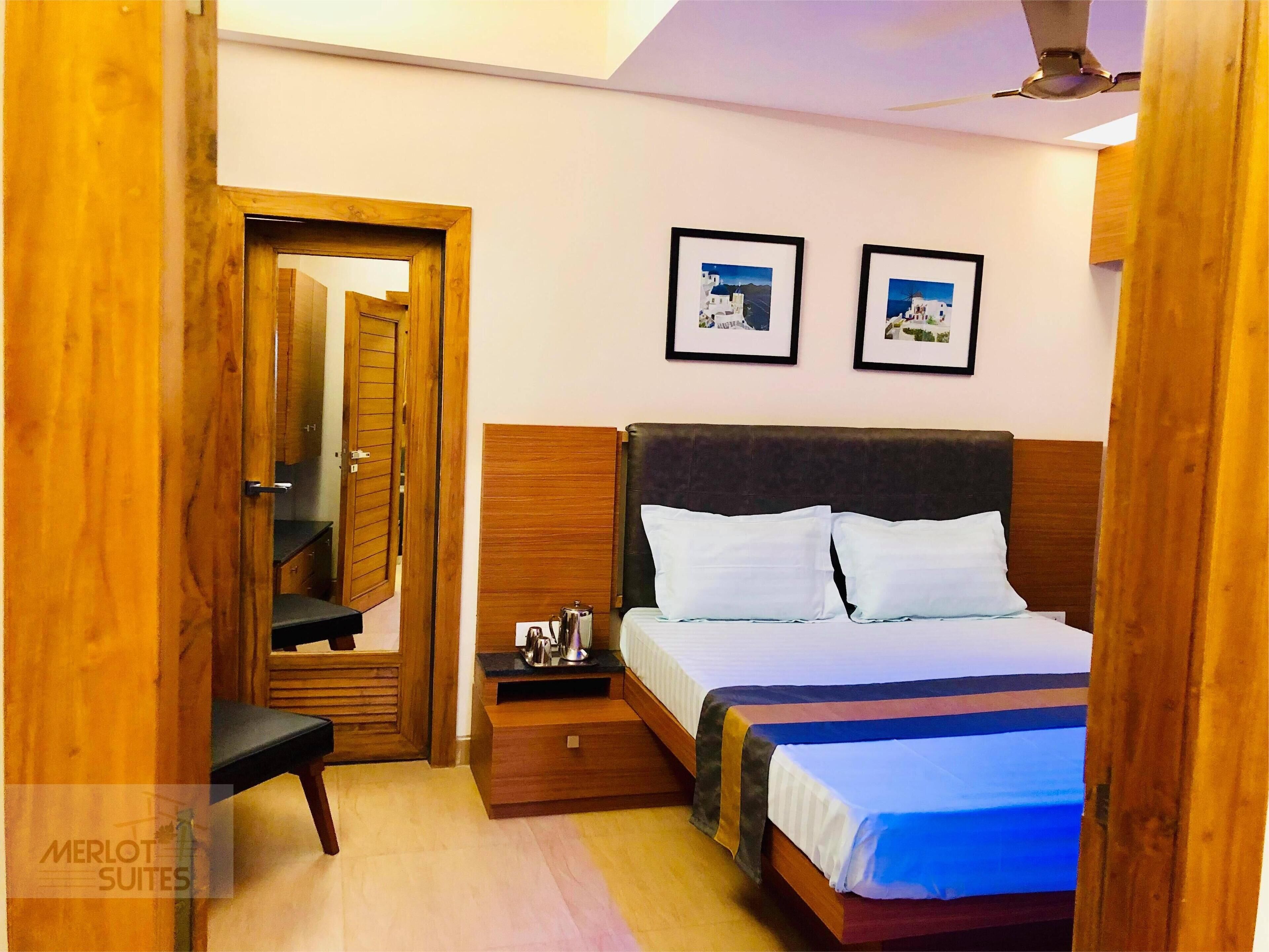 Habitación de hotel con una cama de madera, una mesita de noche, una pequeña mesa y dos cuadros en la pared.