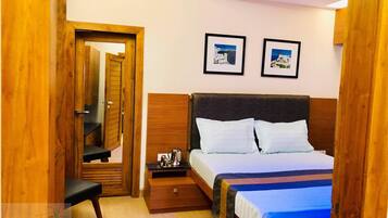 Habitación de hotel con una cama de madera, una mesita de noche, una pequeña mesa y dos cuadros en la pared.
