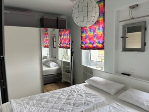 Cozy retreat with a neatly made bed, bedside table, and window with a colorful curtain.