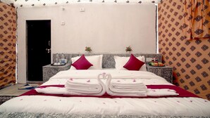 A neatly made bed with towels and a heart-shaped decoration, a nightstand with toiletries, and a door to the left. - Desert Gold Resort (Jaisalmer)