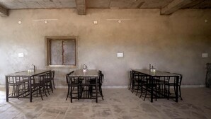 A room with a large, rectangular dining table surrounded by chairs, a window, and a ceiling fan. - Desert Gold Resort (Jaisalmer)
