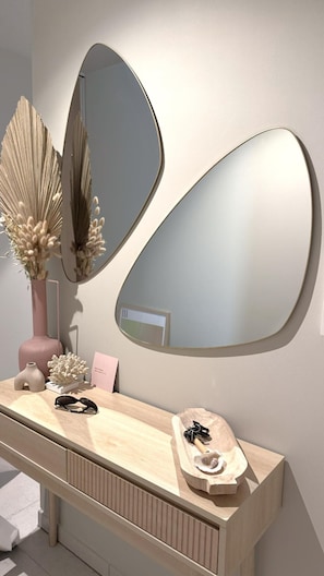 Features a sleek, curved mirror above a light wood vanity with a small decorative tray and a vase with dried flowers.