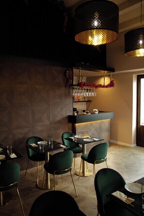 Un ristorante con zona bar, sedie imbottite verdi e lampade a sospensione.