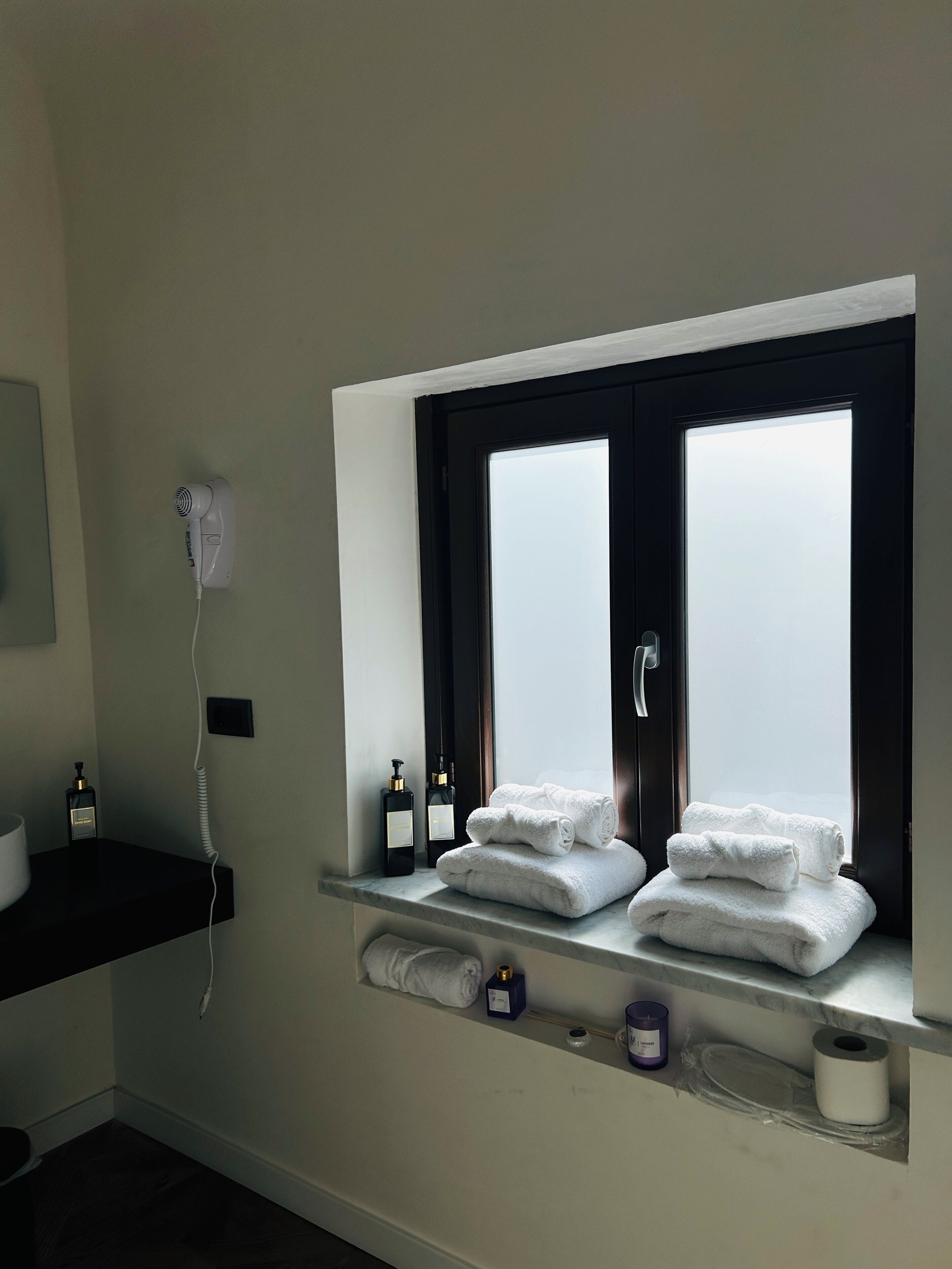 Un bagno con finestra, asciugacapelli e articoli da toilette su uno scaffale.