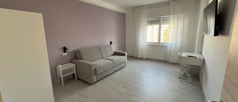 Una sala de estar minimalista con un sofá, una mesita y un televisor montado en la pared.
