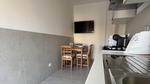 A modern kitchen with a stainless steel sink, a flat-screen TV mounted on the wall, and a dining area with wooden chairs and a table. - Sve's House (Roma)