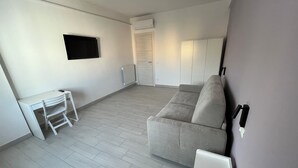 A modern living room with a grey sofa, a white table with a chair, a mounted TV, and a radiator. - Sve's House (Roma)