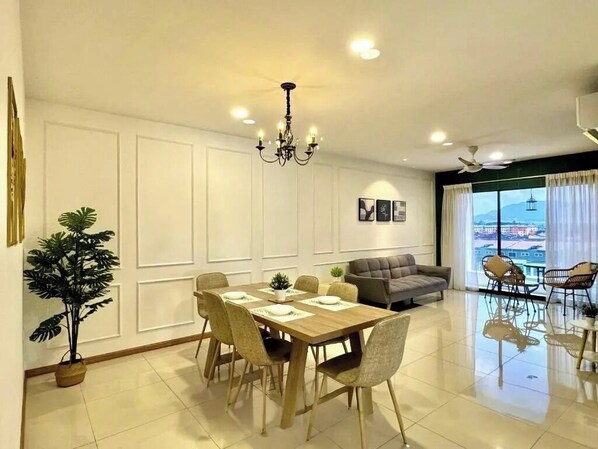 Uma sala de jantar moderna com mesa e cadeiras de madeira, um lustre e um sofá ao fundo.