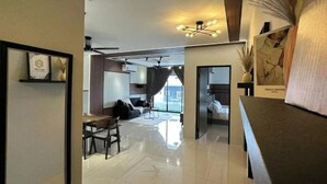 Una sala de estar moderna con sofá, mesa de comedor y sillas. Se observa un área de cocina al fondo con una ventana.