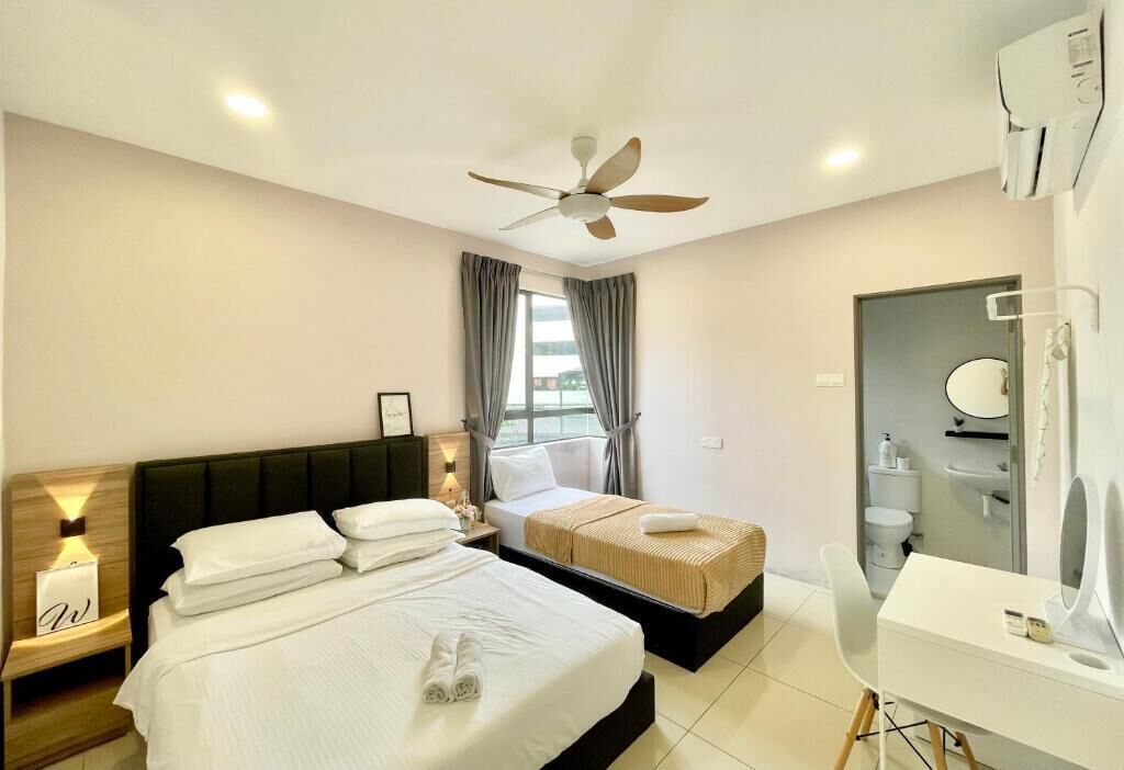 A hotel room with two beds, a ceiling fan, a bathroom with a mirror, and a desk with a chair.